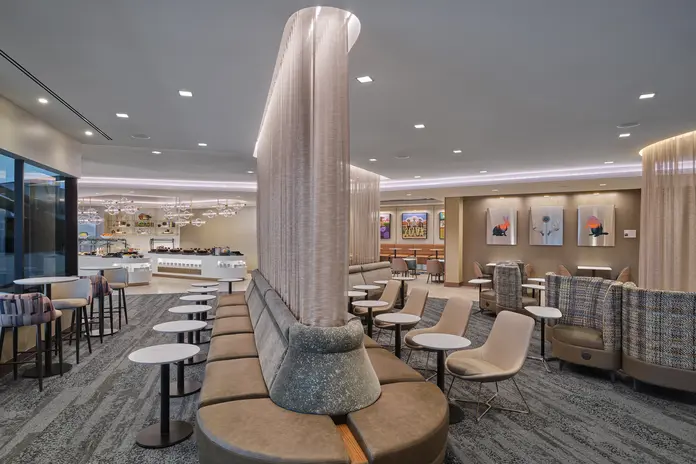 Spacious central area of lounge with curved privacy dividers, varied seating areas, small round tables and a buffet area in the background