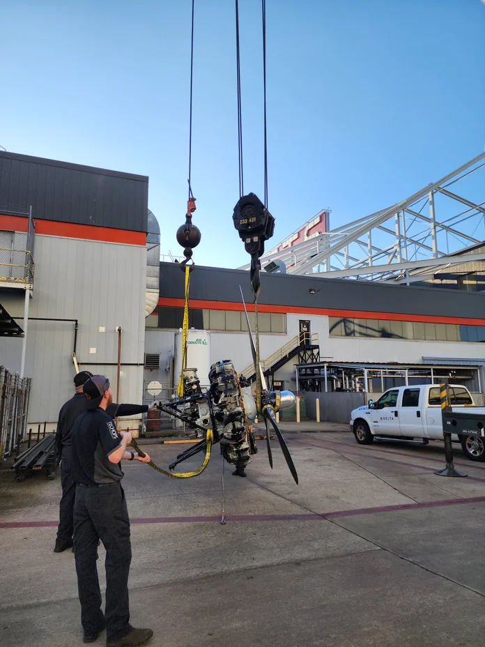 Workers use a crane to lift an aircraft engine and propeller assembly