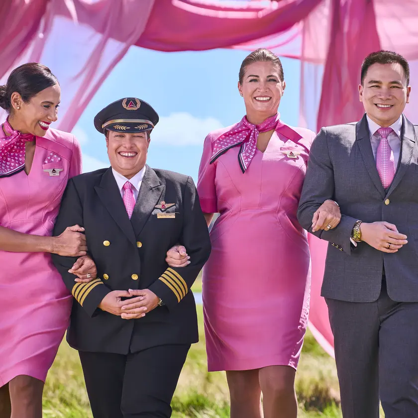 Four Delta employees in pink uniforms walking arm in arm