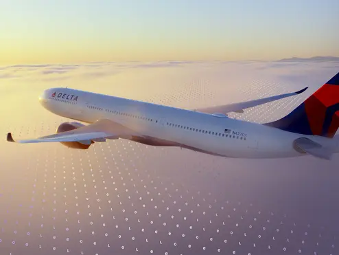 A Delta jet flies above a cloud layer at sunset, with a faint digital grid pattern overlaid across the sky.