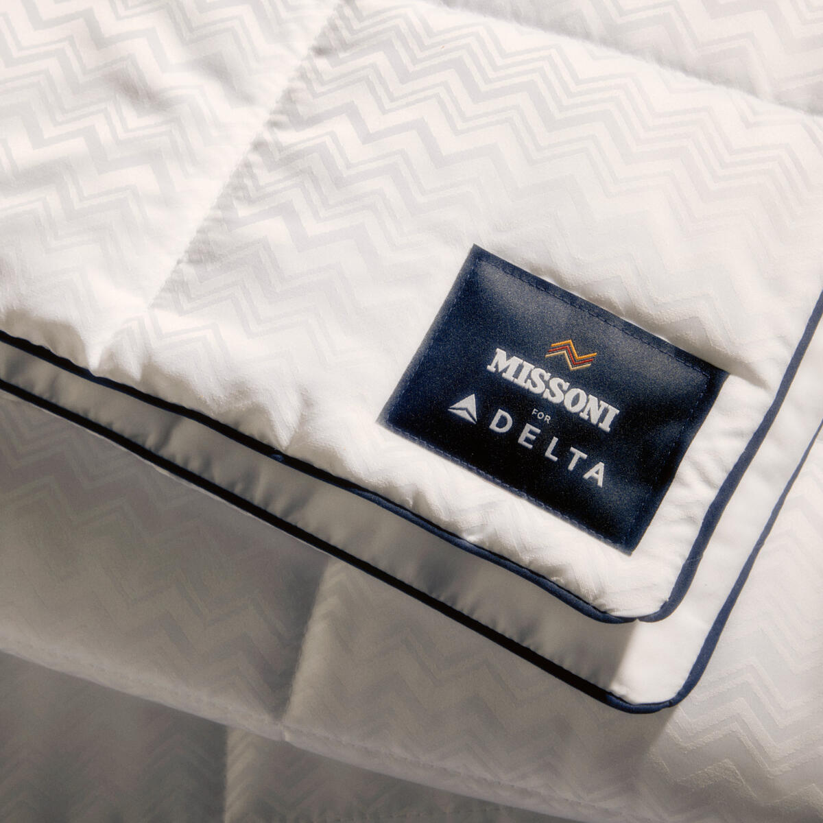 El nuevo juego de cama de Delta One incluye el edredón Missoni y una almohada blanca para dormir, con un sutil y elegante diseño en zigzag de Missoni y detalles en azul marino.