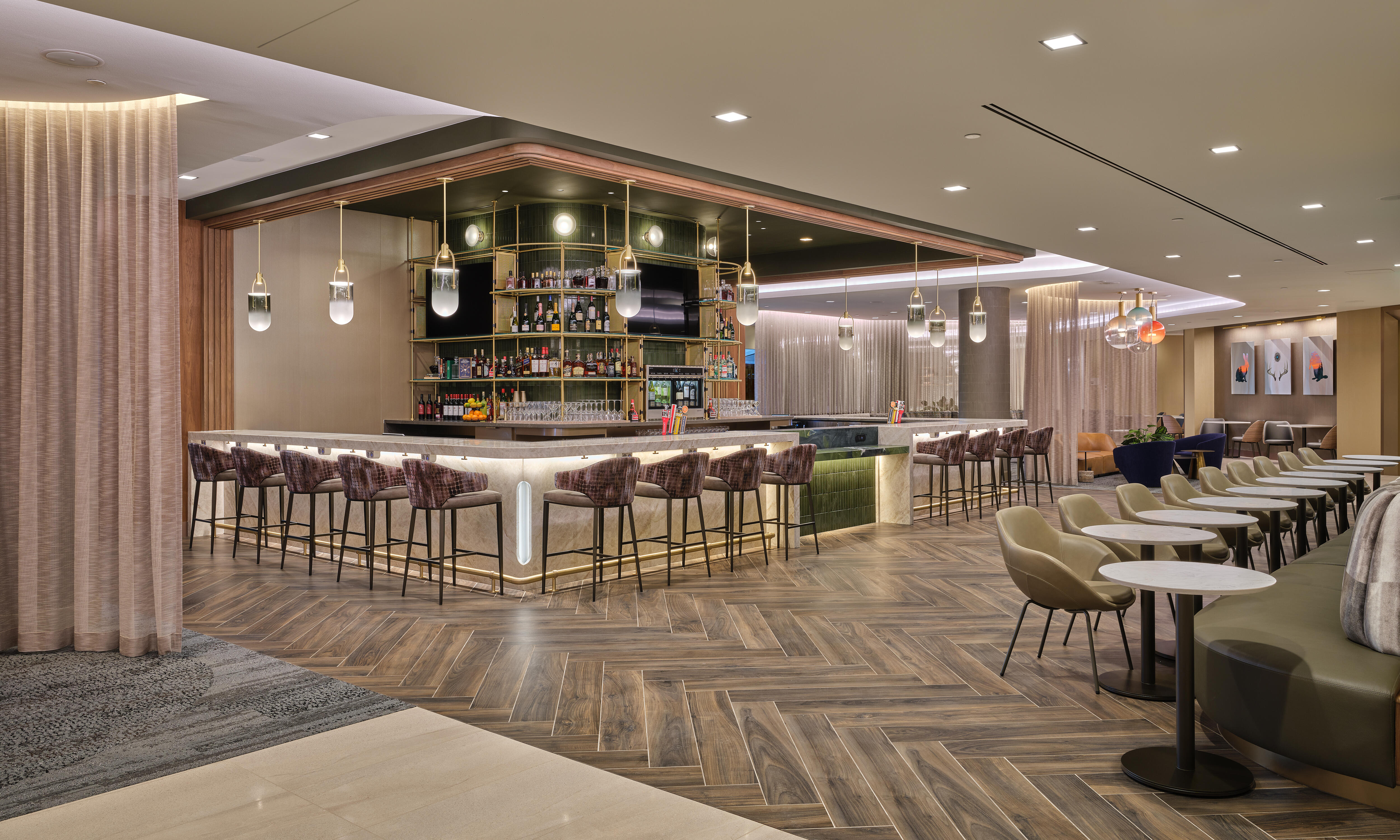Lounge bar with high‑back stools, illuminated shelving, warm lighting and adjacent seating areas with small tables