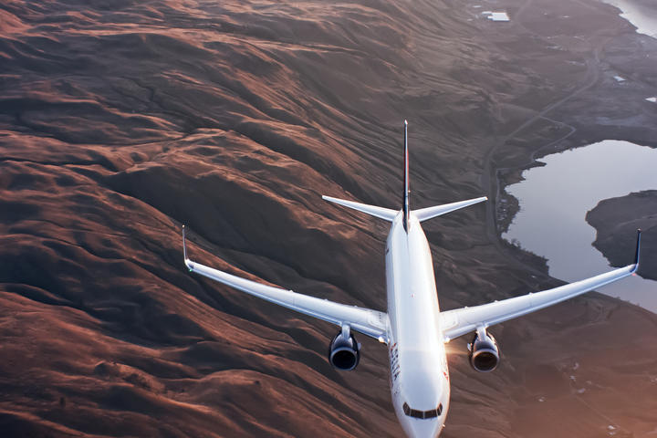 A 737-900 flies over mountains and a river.