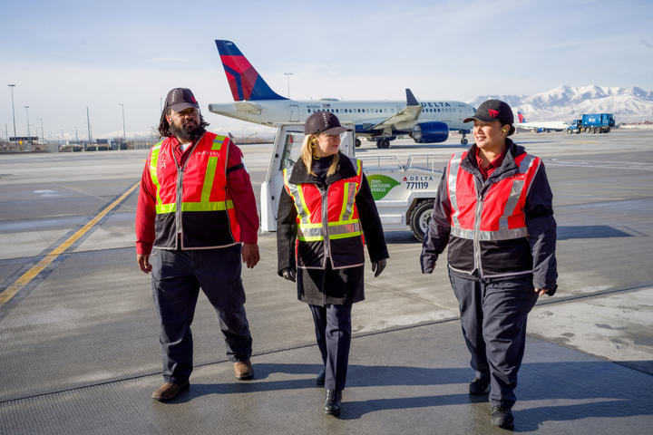Delta Chief Sustainability Officer Pam Fletcher (middle) talks with Aircraft Load Agent Thomas Tuikolovatu (left) and Ramp Agent Sinai Pauni (right) about how they use eGSE at Salt Lake City International Airport (SLC).