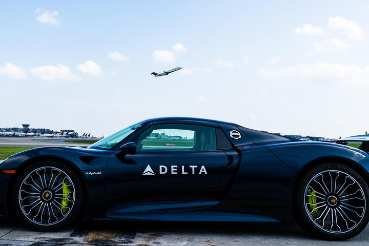 A Delta Boeing 717 takes off above a Porsche 918 Spyder at Hartsfield-Jackson Atlanta International Airport.