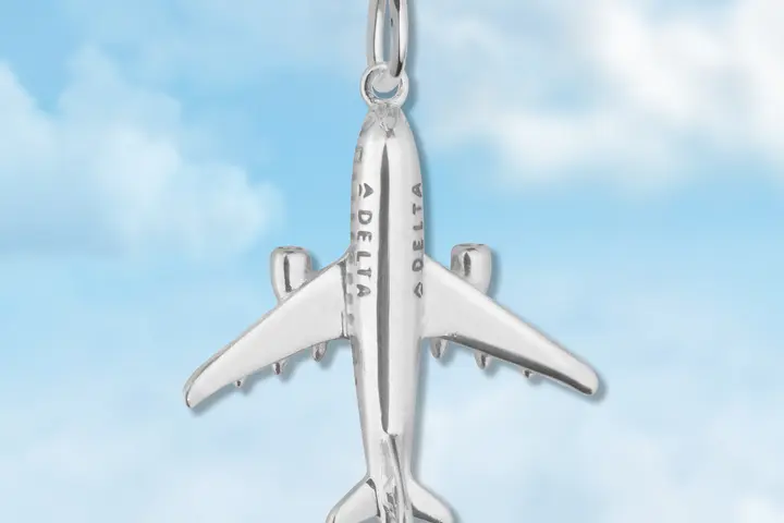 Silver plane charm on blue cloud background. 
