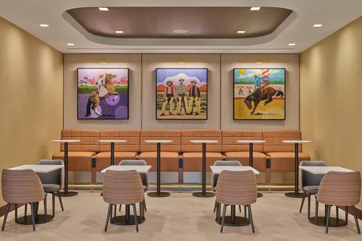 Seating nook with woven chairs, high-back bench seating, small tables and three colorful art pieces displayed on the wall
