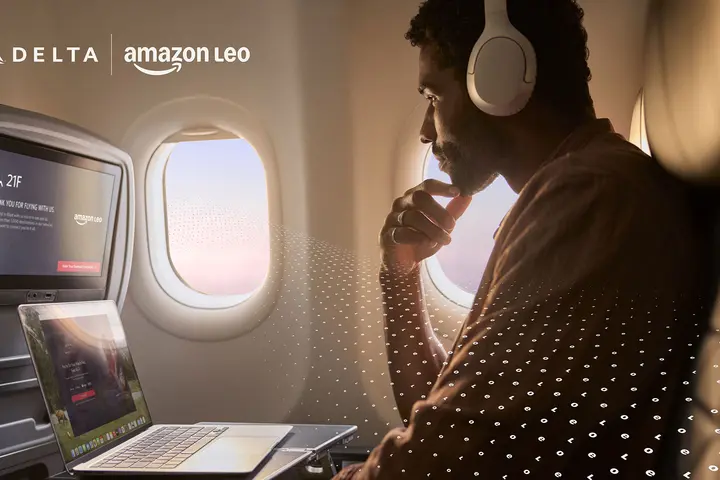  A customer seated by an airplane window uses a laptop and wears over‑ear headphones, with an in‑flight entertainment screen visible and a subtle digital pattern overlay.