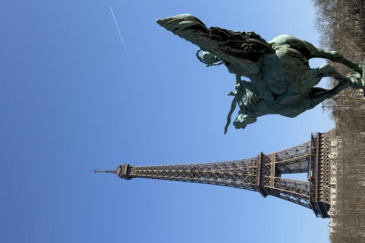 A bronze statue of the winged horse Pegasus is in the foreground, with the Eiffel Tower prominent in the background under a blue sky, viewed from the Pont de Bir-Hakeim.