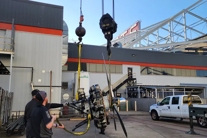Workers use a crane to lift an aircraft engine and propeller assembly