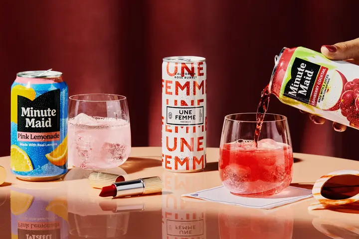 Promotional beverage display featuring Minute Maid Pink Lemonade and Cranberry Cocktail, sparkling rosé, and two iced drinks on a tabletop with lipstick and sunglasses accents.