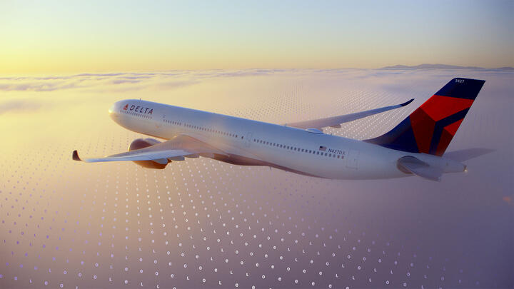 A Delta jet flies above a cloud layer at sunset, with a faint digital grid pattern overlaid across the sky.