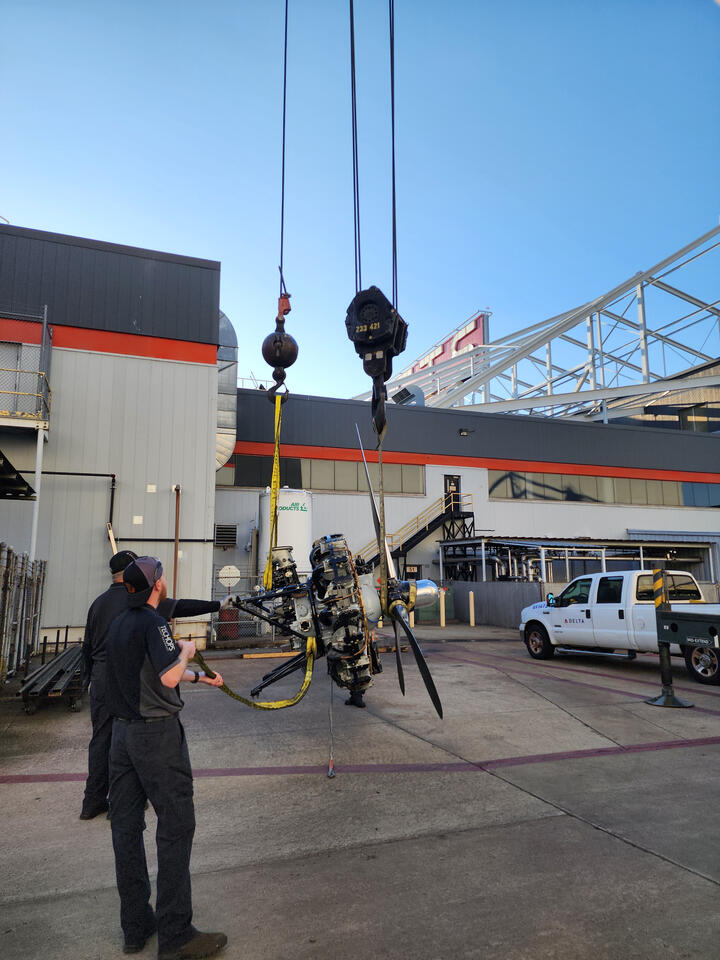 Workers use a crane to lift an aircraft engine and propeller assembly