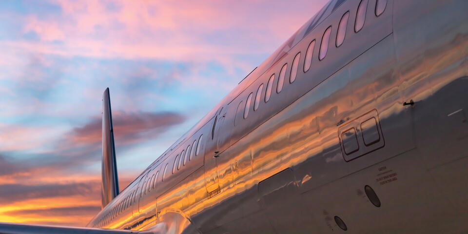 The side of a 757-200 with sunset reflected along with the tail and wing in view.