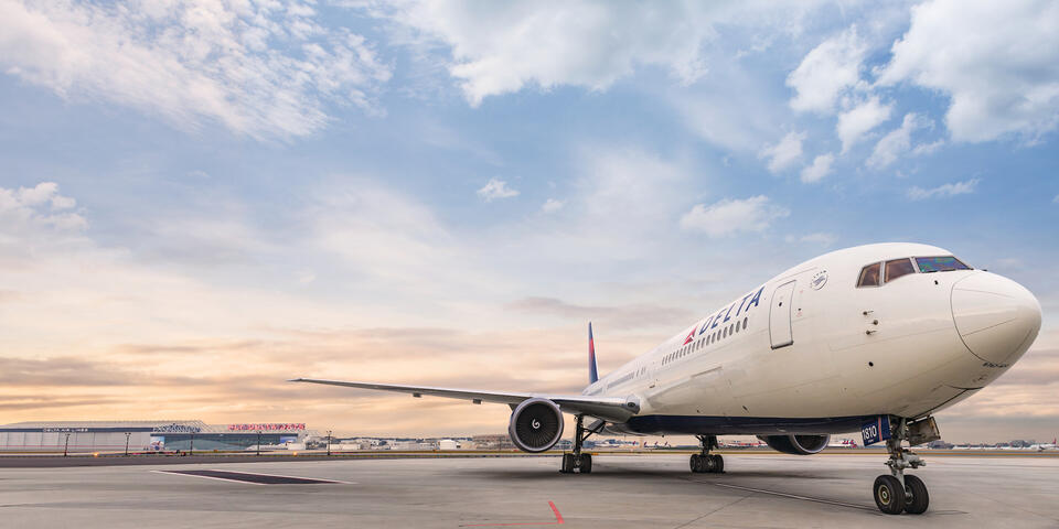 A frontal view of Delta's Boeing 767-400 model sits on the runway while a wisped sky overlooks. 