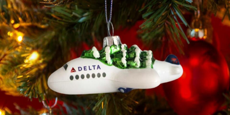 Soar into style with our Festive Delta Plane Ornament. Made of glass with a whimsical tree on top, make sure to snag one before it takes off! 