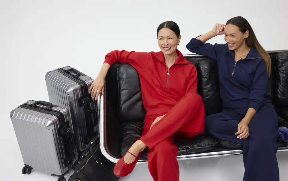 Two smiling women, sitting next to each other dressed in red and navy Spanx outfits.