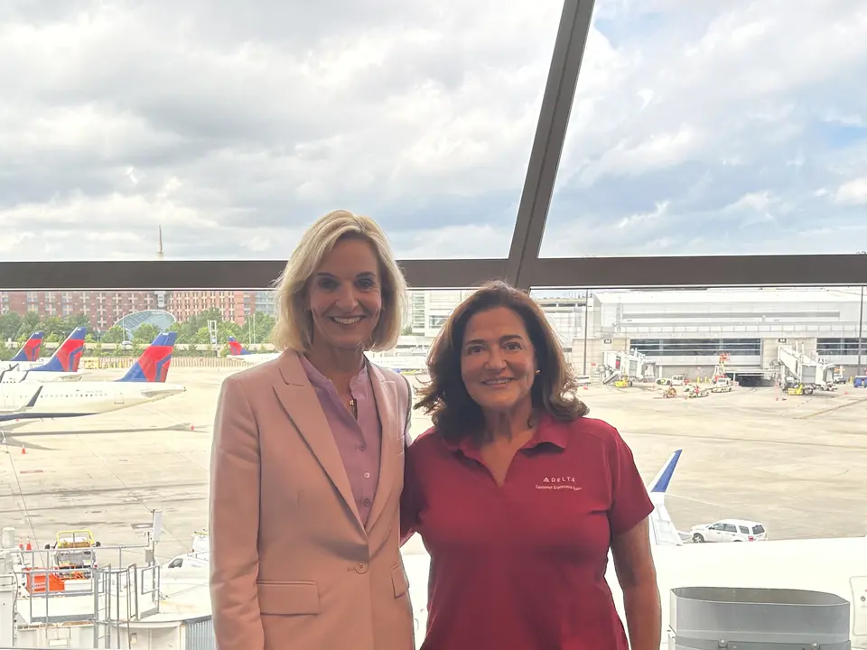 Delta employees Allison Ausband and Nancy Cohn posing against a backdrop of the Boston airport ramp.