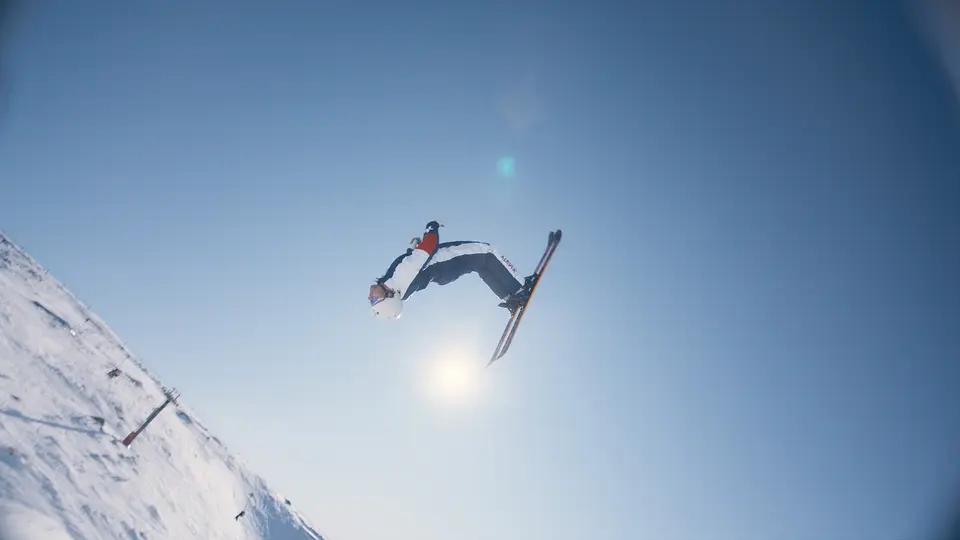 A skier performs a high aerial trick against a clear blue sky on a snowy mountain slope