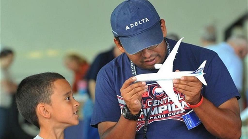 Man holds model airplane while boy looks on.