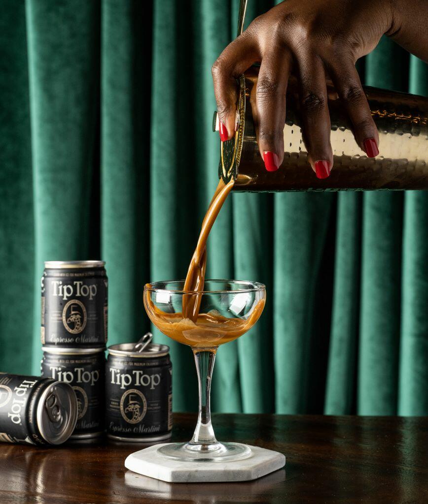 A hand pouring Tip Top Proper Cocktails' Espresso Martini into a martini glass.