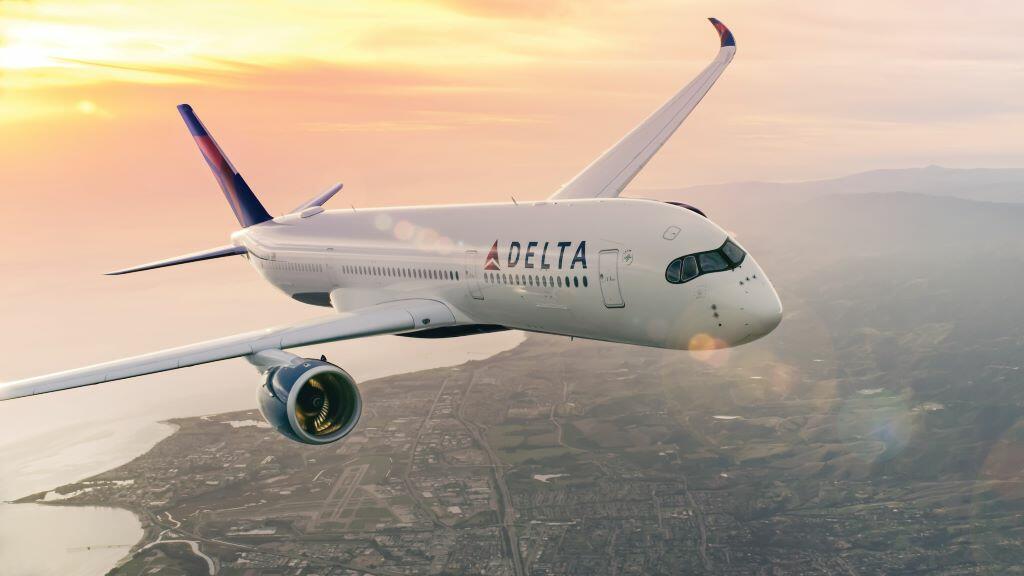 Delta aircraft flying above a coastal city with sun setting in background