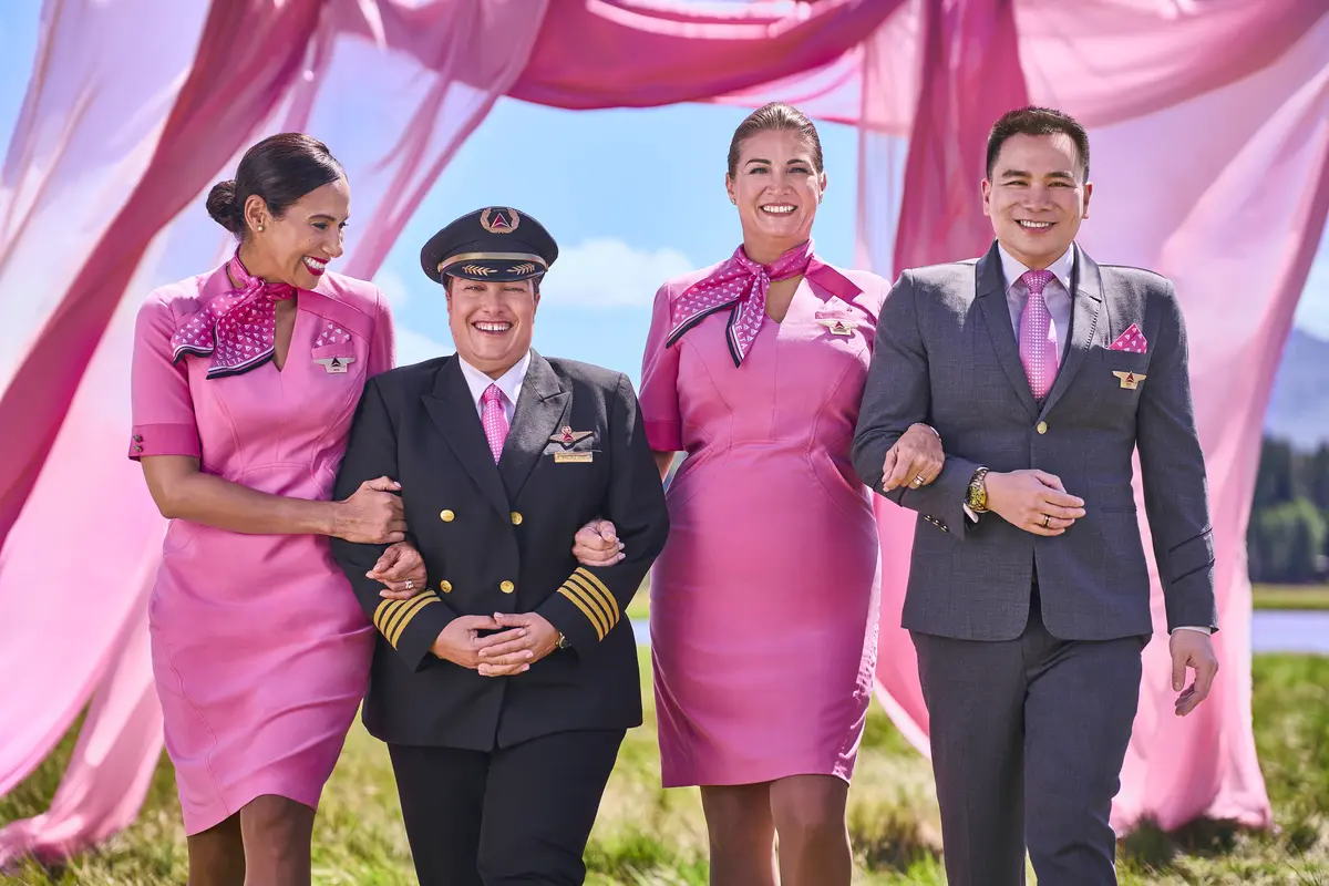 Four Delta employees in pink uniforms walking arm in arm