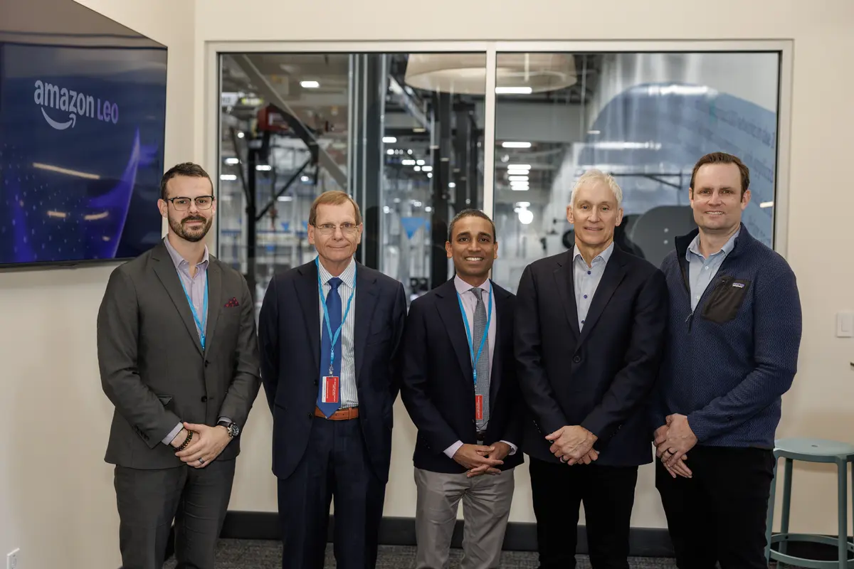 Members of Delta and Amazon Leo teams pose for a picture with factory as backdrop.
