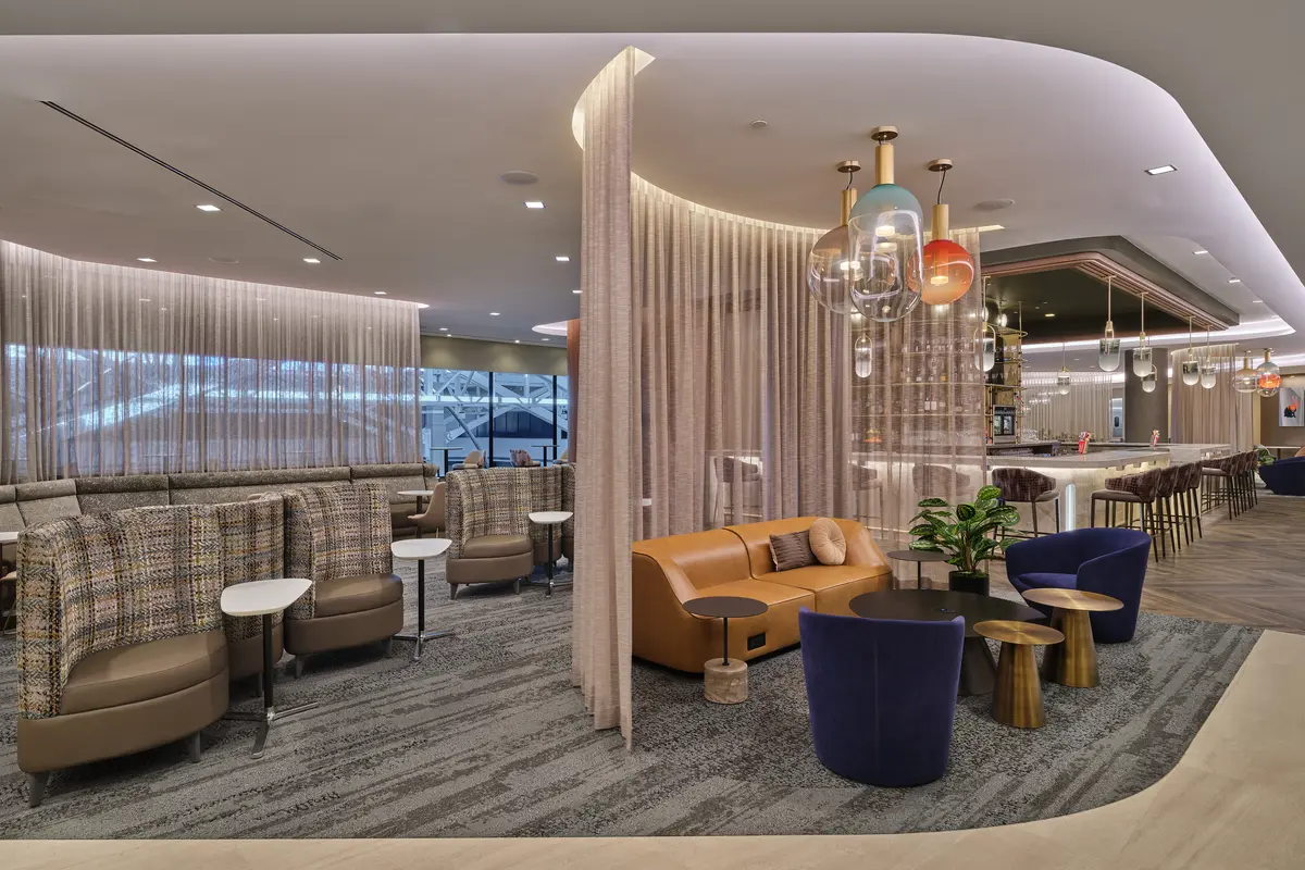 West lounge area with curved seating, soft lighting, privacy curtains and a bar with colorful hanging lights