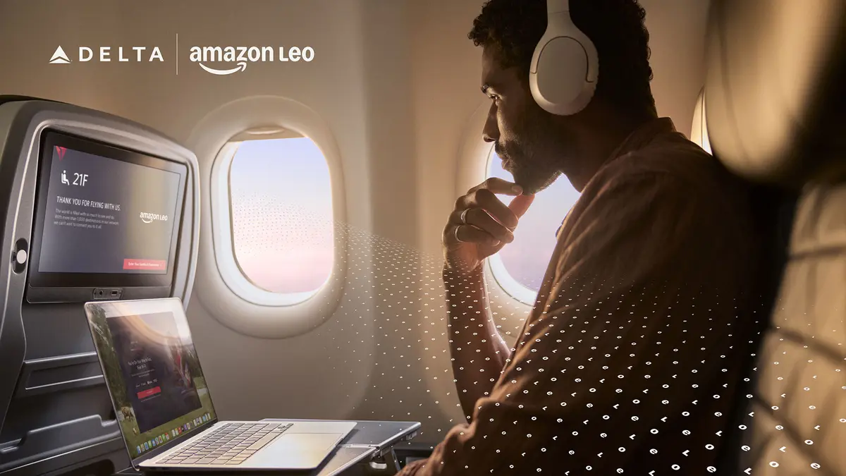  A customer seated by an airplane window uses a laptop and wears over‑ear headphones, with an in‑flight entertainment screen visible and a subtle digital pattern overlay.