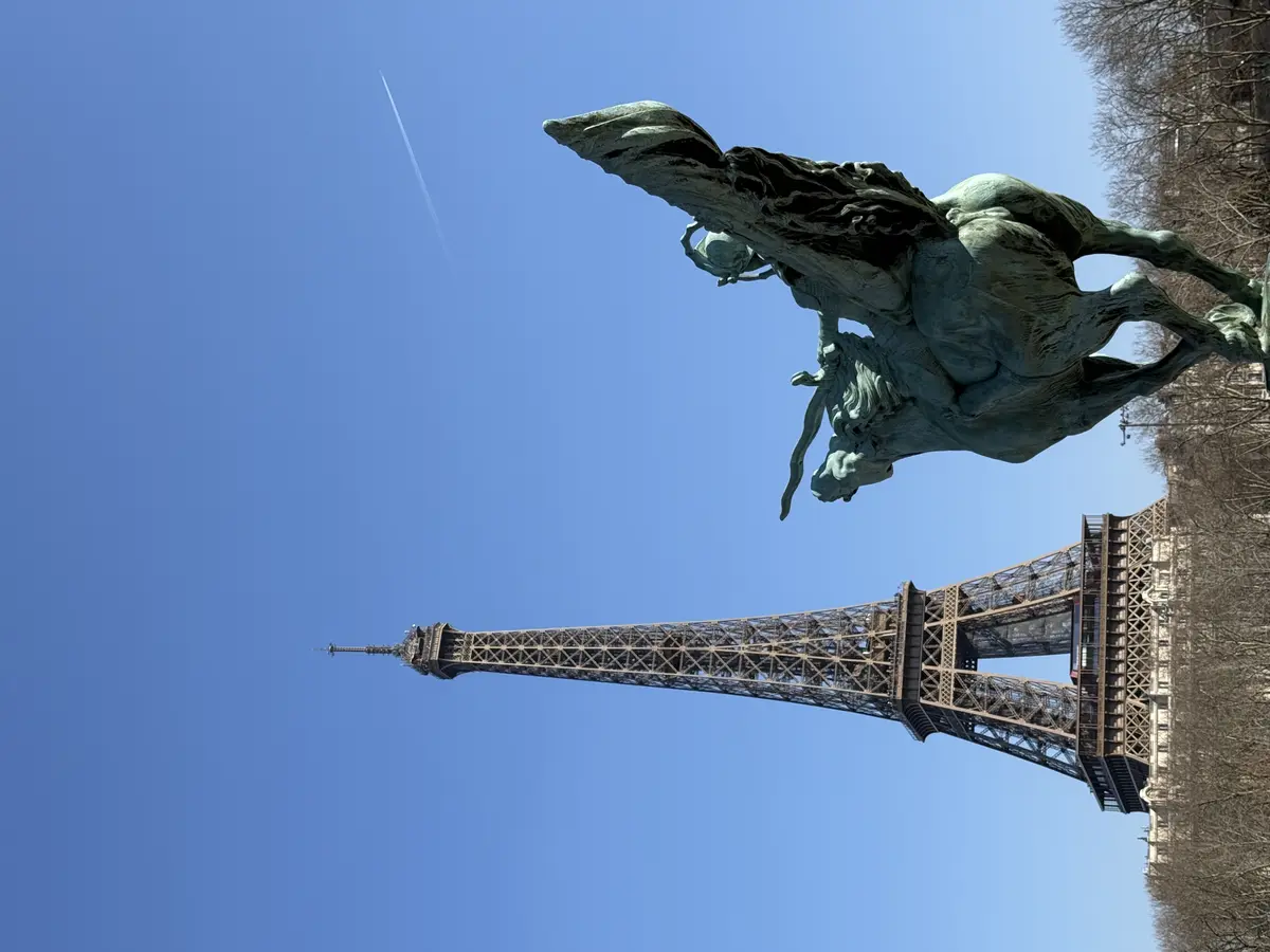 A bronze statue of the winged horse Pegasus is in the foreground, with the Eiffel Tower prominent in the background under a blue sky, viewed from the Pont de Bir-Hakeim.