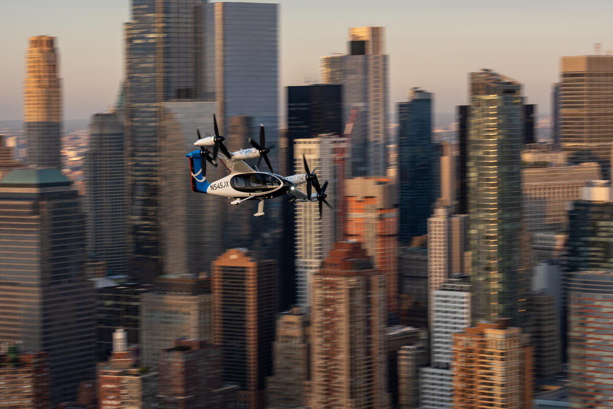 Joby Electric air taxi flying above midtown Manhattan with blurry city skyline in the background.