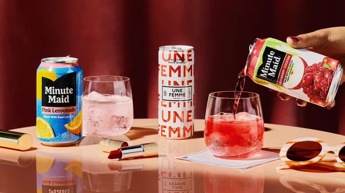 Promotional beverage display featuring Minute Maid Pink Lemonade and Cranberry Cocktail, sparkling rosé, and two iced drinks on a tabletop with lipstick and sunglasses accents.